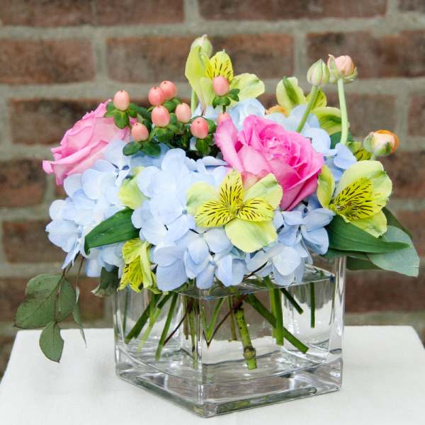 Pink roses and blue hydrangeas in a clear square vase