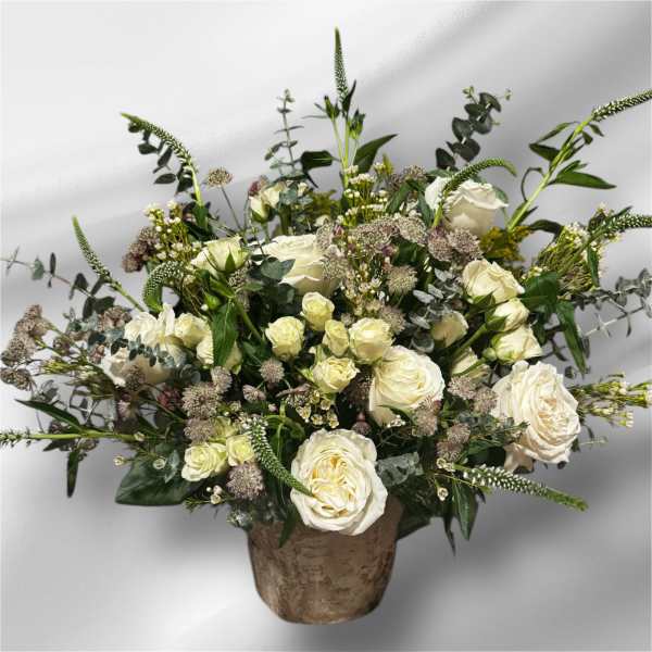 White roses and mixed greenery in a rustic vase