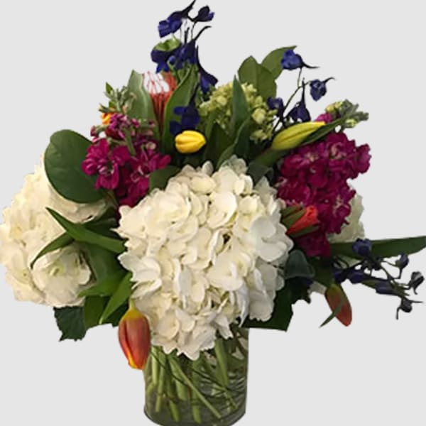 Mixed bouquet with white hydrangeas, purple blooms, and tulips in a glass vase
