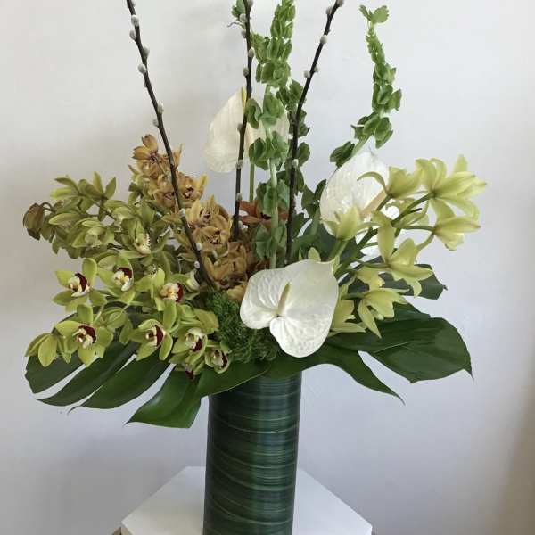 Tall floral arrangement with orchids and white anthuriums in a green vase