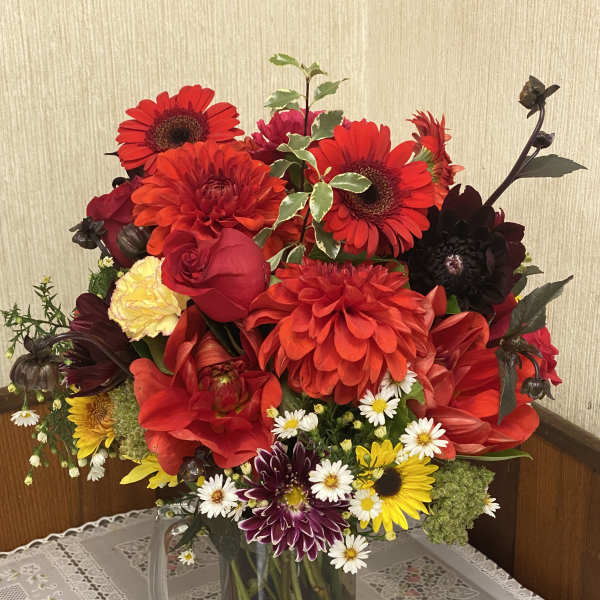 Mixed bouquet of red, yellow, and purple flowers in a glass pitcher
