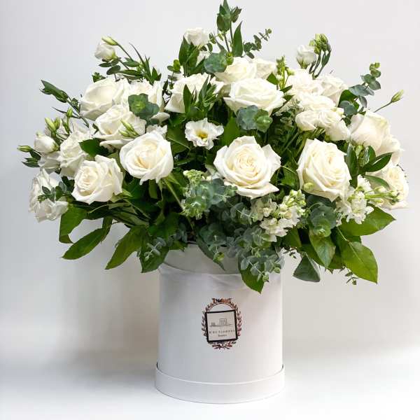 White roses arranged in a white hat box with greenery
