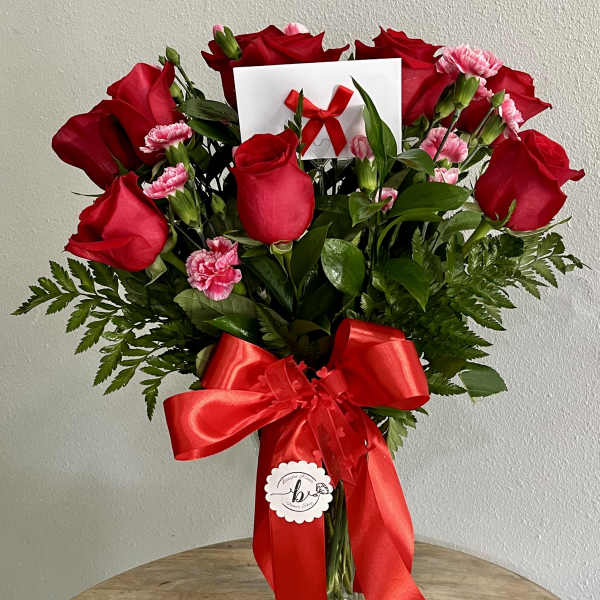 Bouquet of red roses and pink carnations in a glass vase with a red ribbon