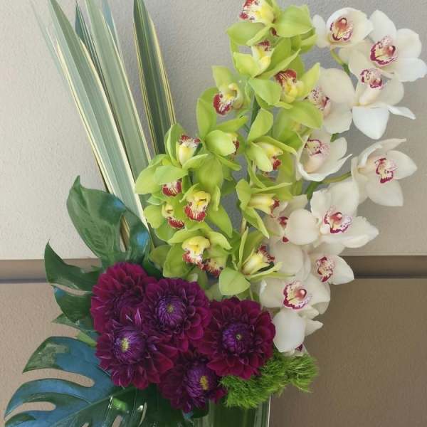 Tall orchid and purple chrysanthemum arrangement in a glass vase