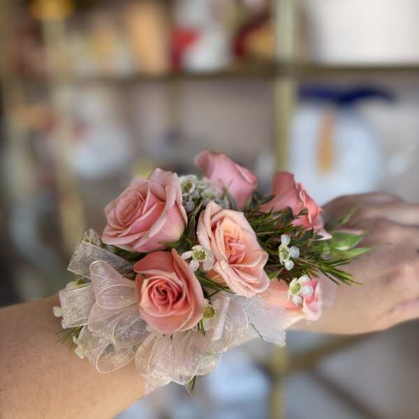 Peach-pink rose wrist corsage with small white blossoms and sheer ribbon on a person's arm