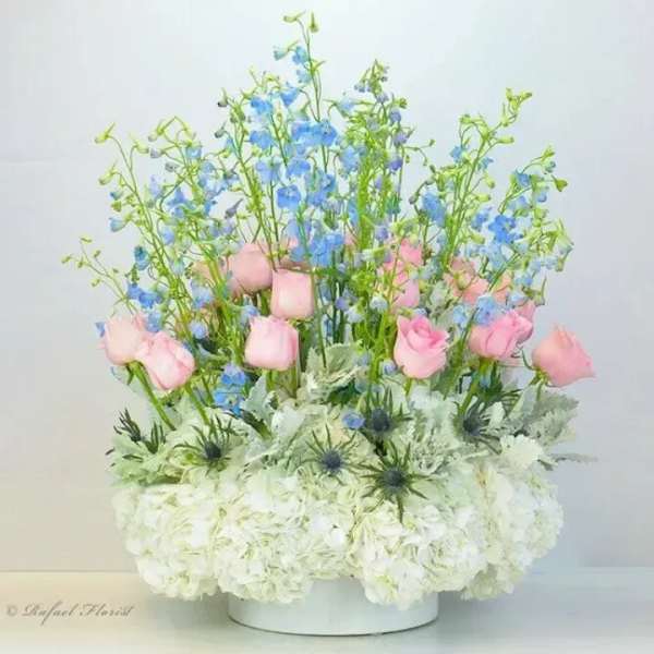 Pink roses and blue delphinium in a white vase with white hydrangeas