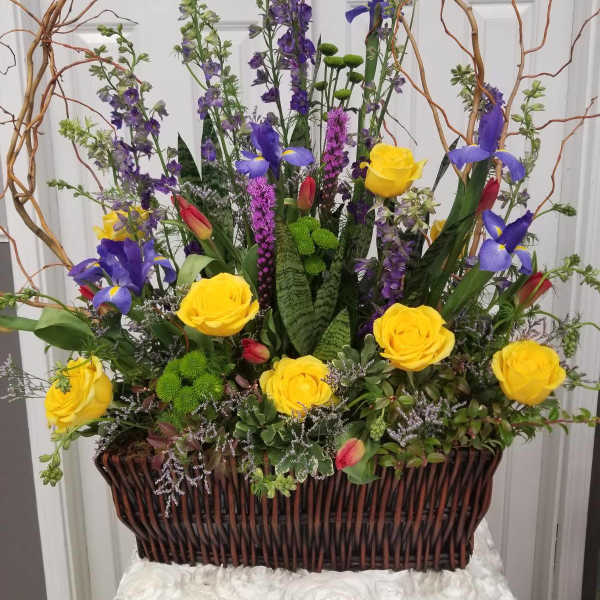 Tall floral arrangement with yellow roses and purple irises in a wicker basket
