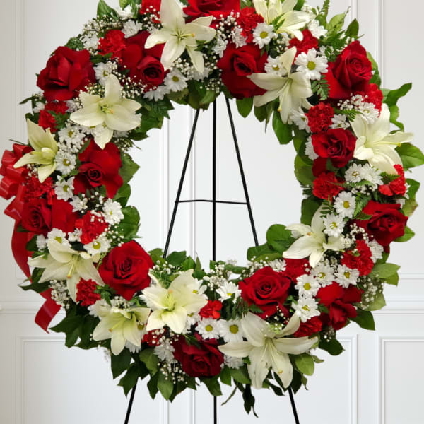Standing wreath of red roses, white lilies, carnations, and daisies on a black metal easel.