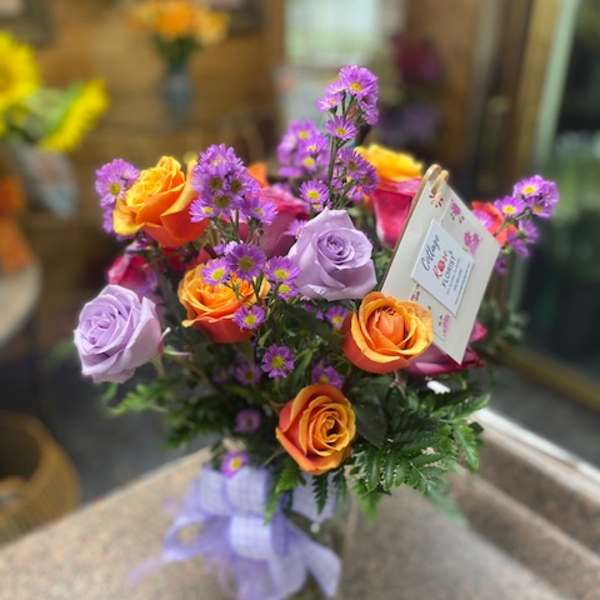 Bouquet of orange and lavender roses with purple filler flowers in a glass vase