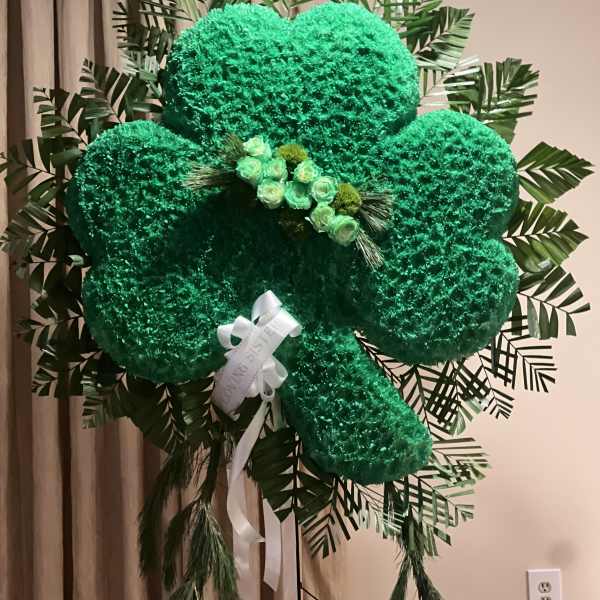Large green floral clover display with a white ribbon and small roses