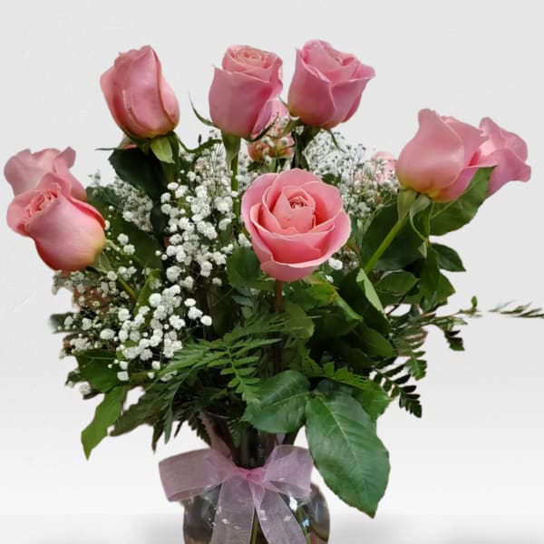 Glass vase of pink roses with white filler flowers and a pink ribbon bow