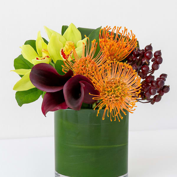 Bouquet of yellow orchids, orange pincushion blooms, and burgundy calla lilies in a green vase
