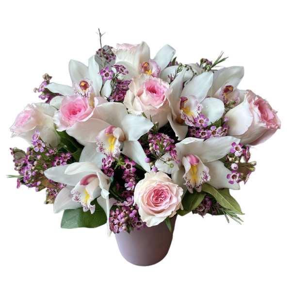 Low arrangement of pink roses, white cymbidium orchids, and tiny purple blooms in a soft pink vase