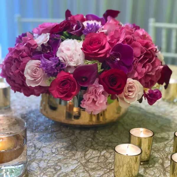 Pink and purple floral centerpiece in a gold vase with candles nearby