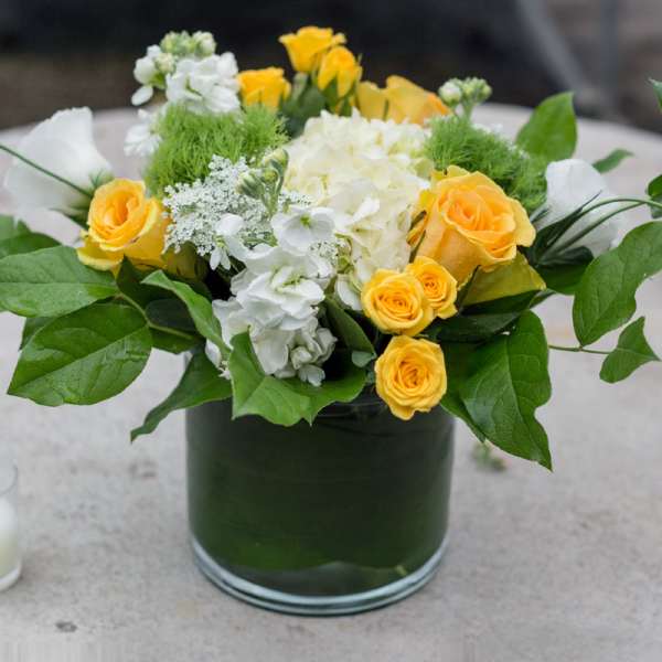 Yellow roses and white flowers arranged in a glass vase