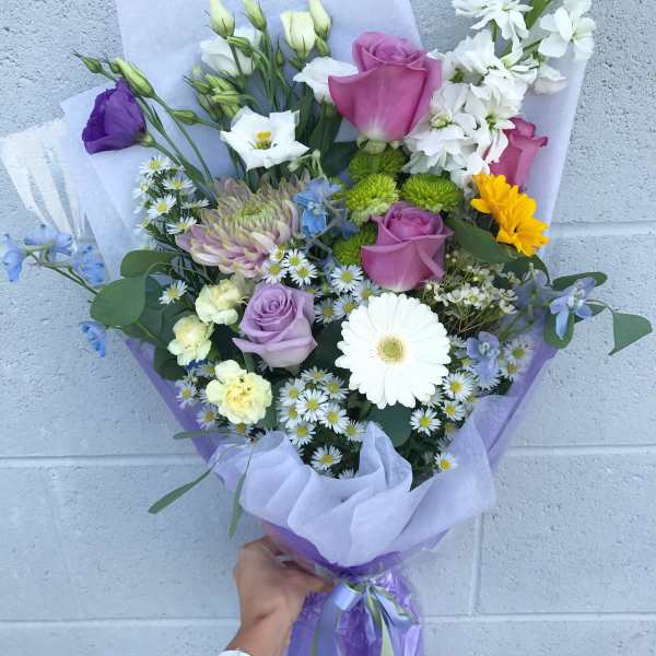 Handheld bouquet of mixed flowers in purple wrapping