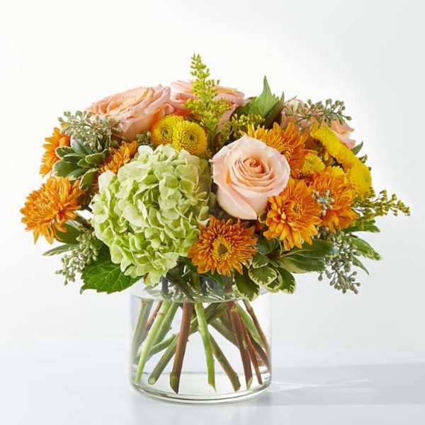 Peach roses and orange mums in a clear glass vase