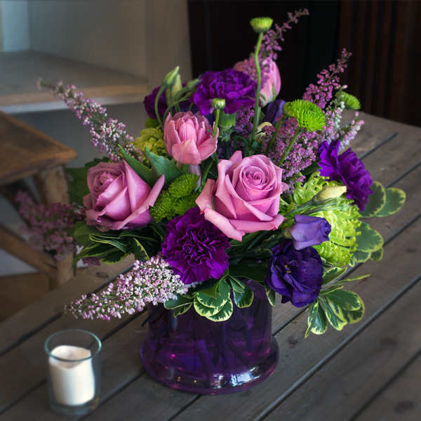 Pink and purple flower arrangement in a purple glass vase