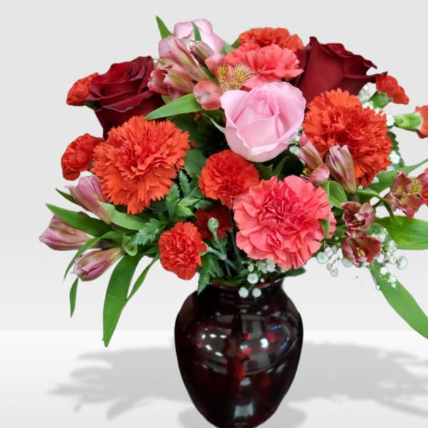 Mixed bouquet of red and pink roses and carnations in a dark red glass vase