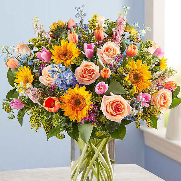 Mixed bouquet of sunflowers, roses, and tulips in a glass vase
