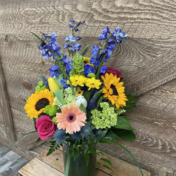 Mixed bouquet in a glass vase with sunflowers, roses, and blue flowers