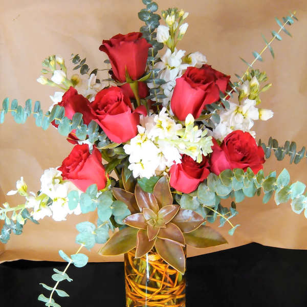 Tall vase arrangement with red roses, white flowers, eucalyptus, and a large succulent.
