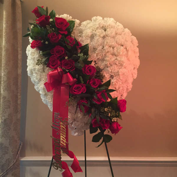 Heart-shaped floral tribute with red roses and white flowers on a stand