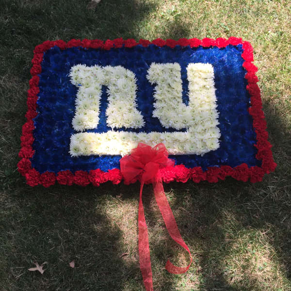 Rectangular floral tribute with white lettering, red border, and a red ribbon bow