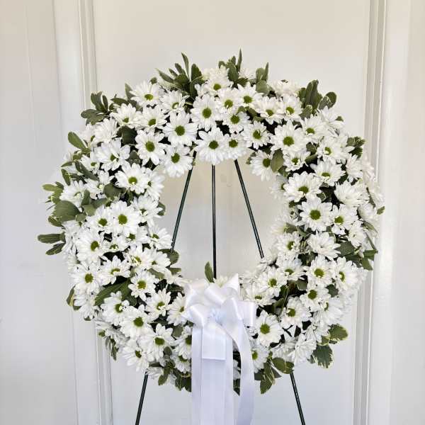 White daisy wreath on a stand with a white ribbon