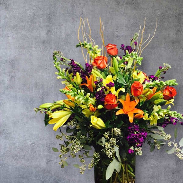 Tall mixed bouquet with orange roses, lilies, and purple flowers in a glass vase