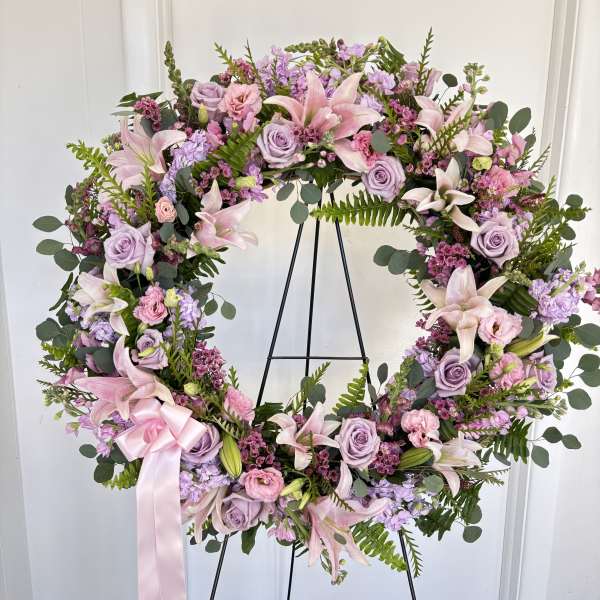Lavender and pink floral wreath on a black stand with a pink ribbon