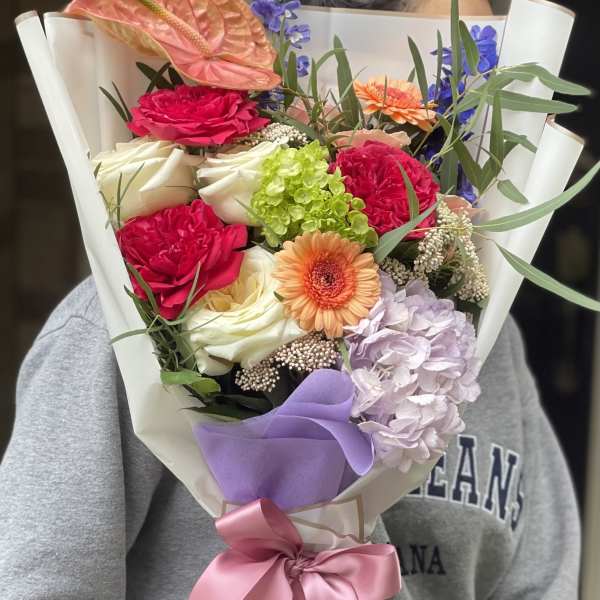 Bouquet of mixed flowers wrapped in white paper with a pink ribbon