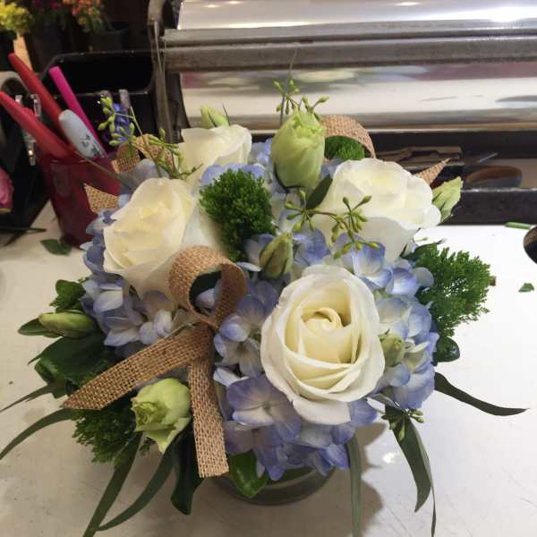 White roses and blue hydrangeas in a glass vase with burlap ribbon