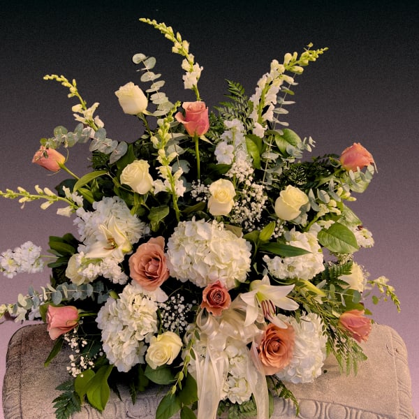 Large floral arrangement with white hydrangeas, roses, and lilies in soft pink and cream.