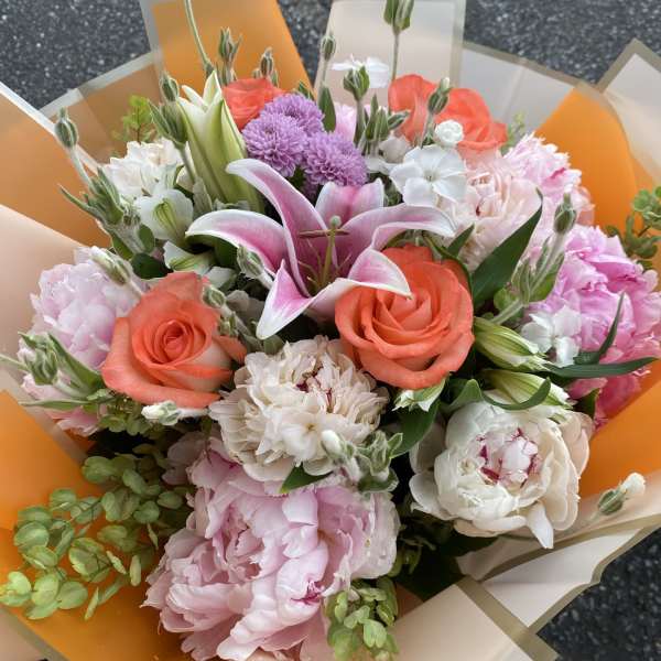 Mixed bouquet with pink lilies, coral roses, and white blooms wrapped in orange paper
