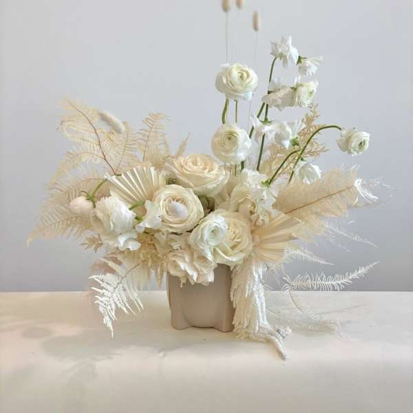 Cream floral arrangement in a beige vase with tall stems and dried accents