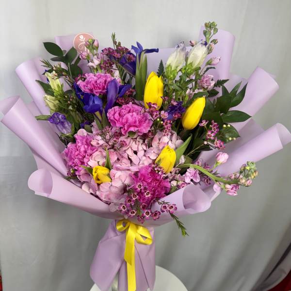 Bouquet of pink, yellow, and purple flowers wrapped in lavender paper