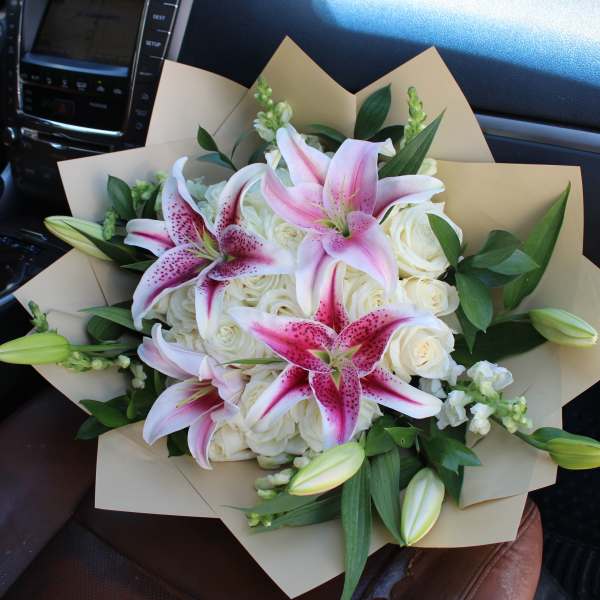 Bouquet of pink lilies and white roses wrapped in tan paper