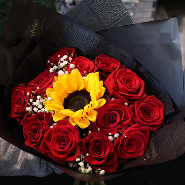 Bouquet of red roses with a yellow sunflower in black wrapping