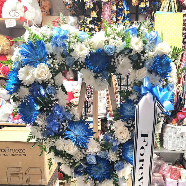 Blue and white floral heart wreath on a wooden easel with a memorial ribbon
