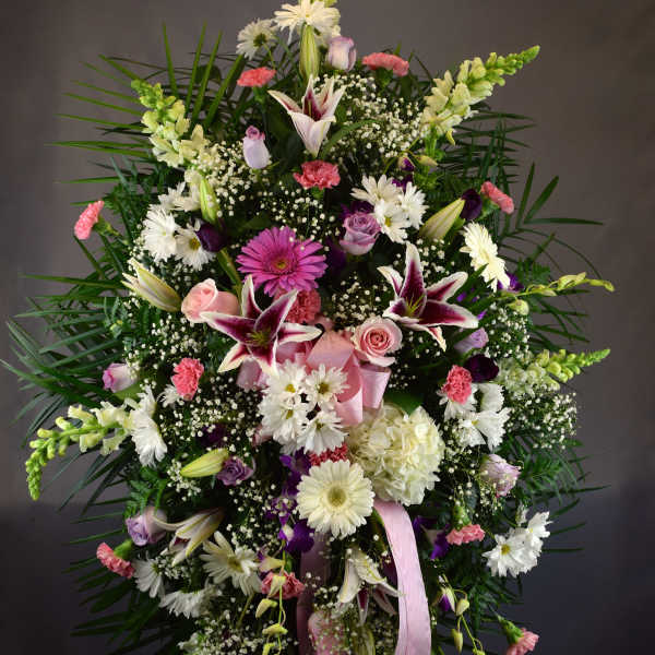 Large standing floral spray with lilies, daisies, roses, and pink ribbon