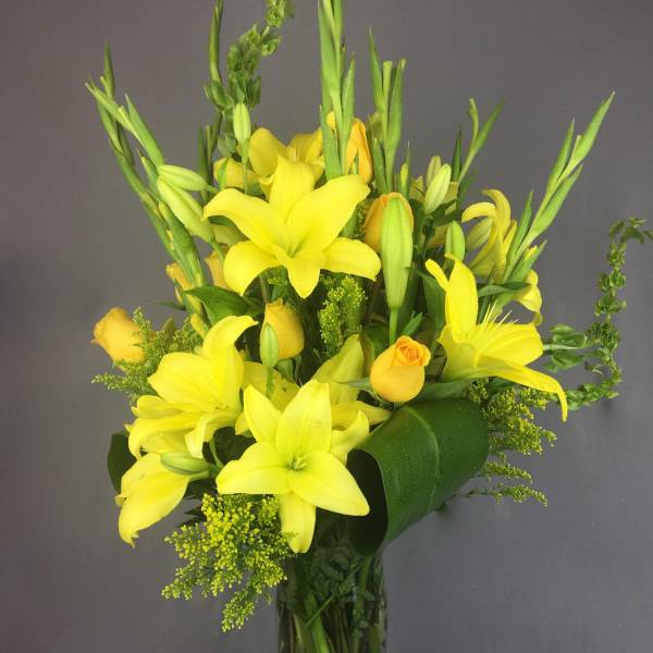 Yellow lilies and roses arranged in a clear glass vase
