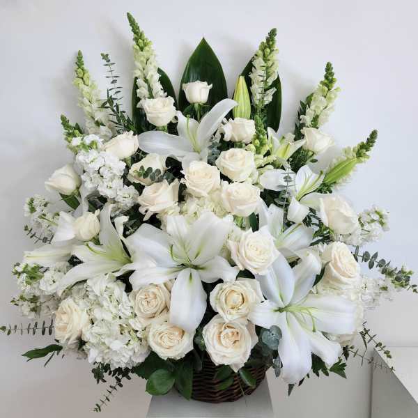 White roses and lilies arranged in a basket with tall white spikes.
