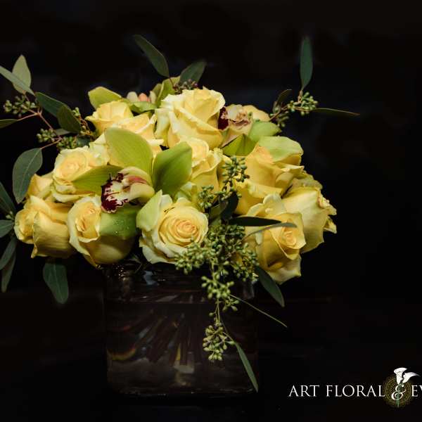 Yellow rose bouquet in a glass vase with green foliage