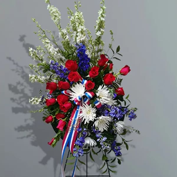 Standing floral spray with red roses, white daisies, and blue flowers on an easel