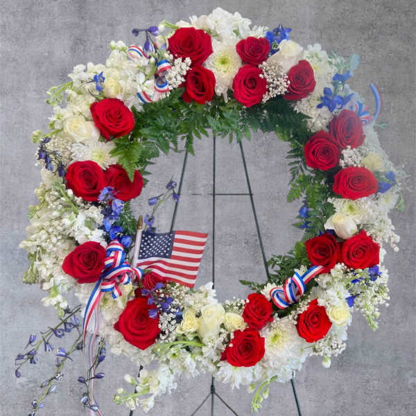 Red, white, and blue floral wreath on a stand with an American flag