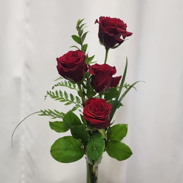 Four red roses in a clear glass vase with greenery