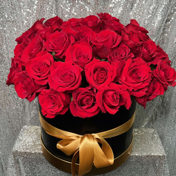 Red roses arranged in a black round box with a gold ribbon