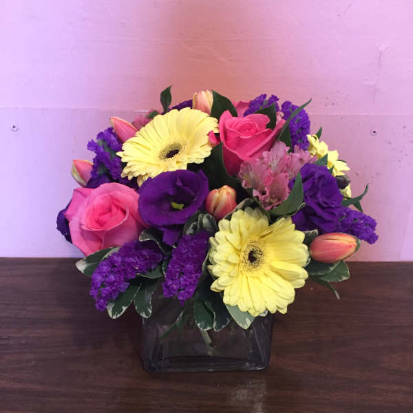 Pink roses and yellow gerbera daisies in a square glass vase