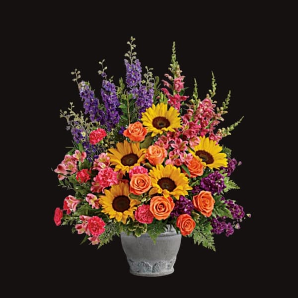 Colorful bouquet of sunflowers, orange roses, and pink-purple blooms in a gray vase